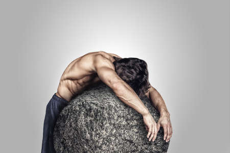 Shirtless sporty male ebracing big stone.の写真素材