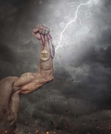Male hand holding gold medal against the dramatic skyの写真素材