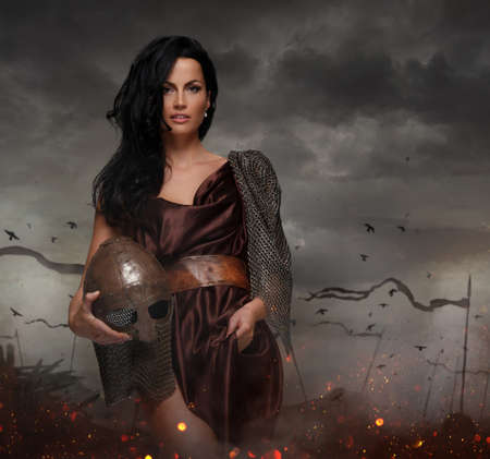 Attractive war queen holding helmet in fire sparks on a battle field.の写真素材