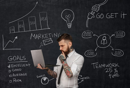 Tattooed bearded techer with laptop over school desk with formulas.の写真素材