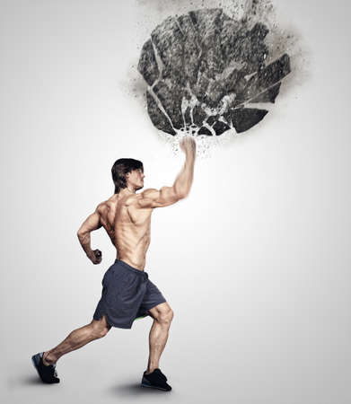 Shirtless athletick male kicking big grey rock. Studio shoot. Isolated on a grey background.の写真素材