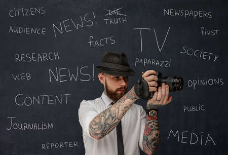 Bearded dslr photographer with tattooes on his arms over school desk background.の写真素材