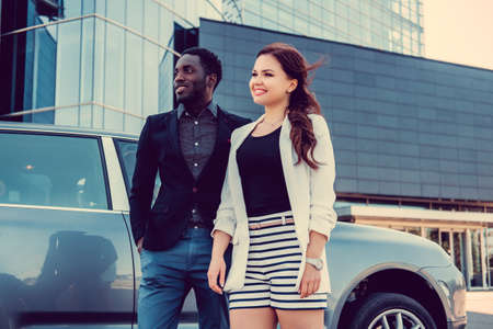 Casual african american man and caucasian business lady posing near a car.