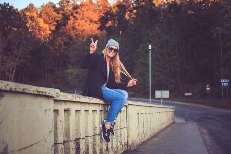 Blond female in denim jeans and sunglasses sitting on a bridge in nature national park.の写真素材