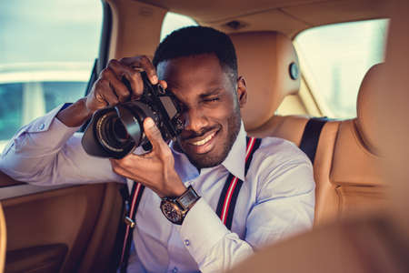 African american male in a white shirt shooting with dslr camera from car's back seat.の写真素材