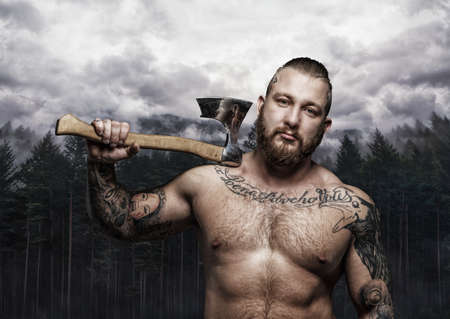 Shirtless tattooed viking holding axe over wild nature background.の写真素材