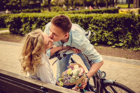 Casual male kissing blond female and presenting her with flowers.