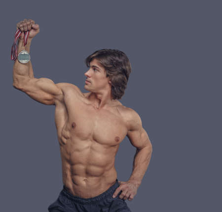 Shirtless muscular male holding silver medal over grey background.の写真素材