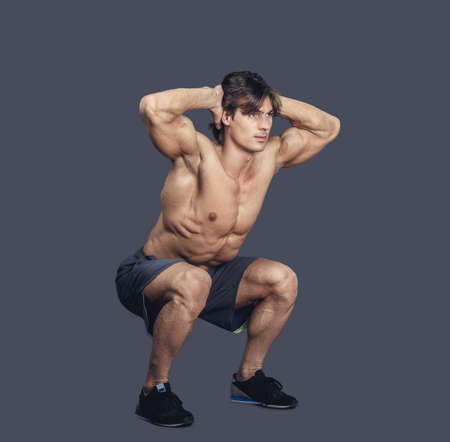 Shirtless muscular male in shorts doing squats. Isolated on grey background.の写真素材