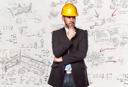 Project manager in a suit with hard yellow helmet over desk with drawnings.の写真素材