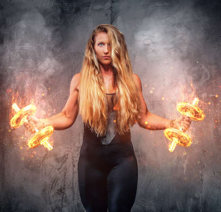 Fitness female model with burning dumbbells in a smoke.の写真素材