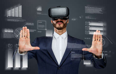 Male in a suit with virtual reality glasses on his head working in virtual financial world.の写真素材
