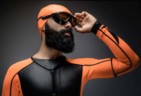 Portrait of bearded male in scuba diving mask and orange neopren diving suit isolated on grey background.の写真素材