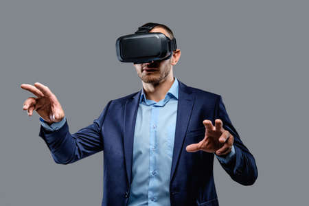 Male in a suit with virtual reality glasses on his head. Isolated on grey background.