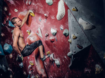 Shirtless athletic male climbing on a red indoor climbing wall.の写真素材