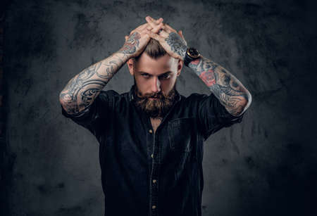 The bearded tattooed male holding head on grey background.の写真素材