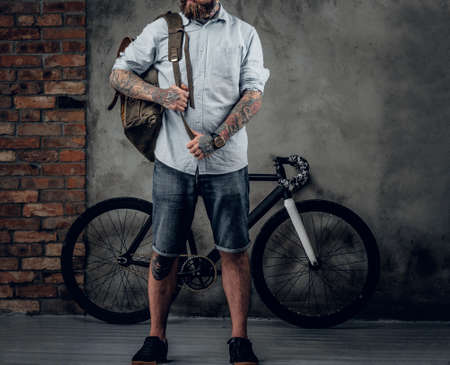 Portrait of bearded hipster male with bag and bicycle on concrete wall background.の写真素材