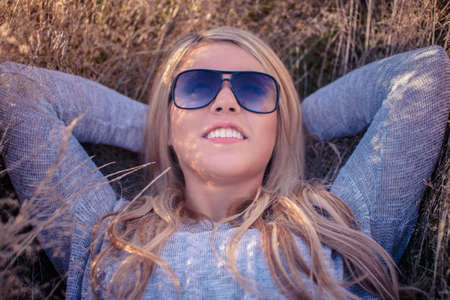Smiling blond female in sunglasses lying on a grass on sunset.