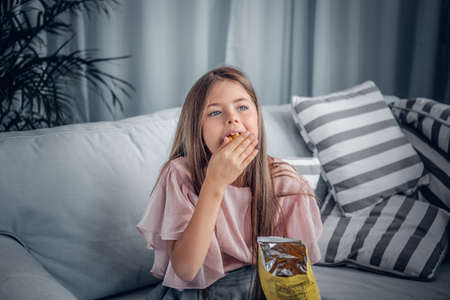 A girl eating candies sitting on a sofa in a living room.の写真素材