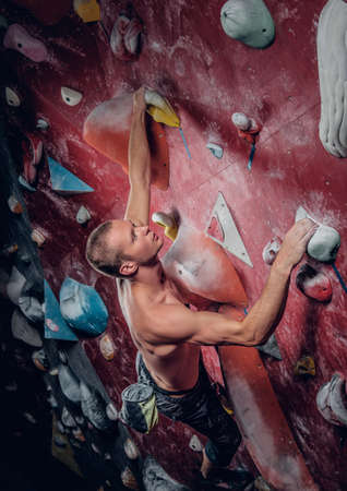 Shirtless athletic male climbing on a red indoor climbing wall.の写真素材