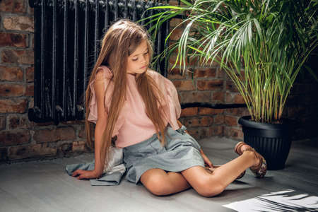 Full body portrait of a girl sits on a floor in a living room in natural light.の写真素材