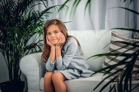 Portrait of a girl posing on a sofa in a living room with green plants.の写真素材