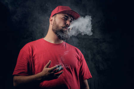 Fatty bearded hipster male in a red hip hop clothes smoking a cigarette on a grey background.の写真素材