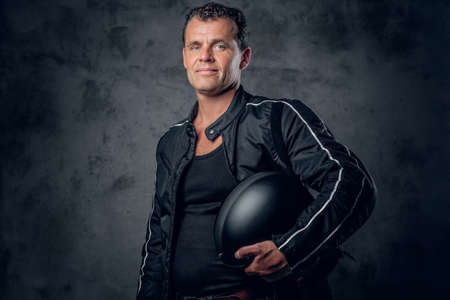 Portrait of middle age biker in sports jacket, holds motorcycle helmet on grey background.の写真素材