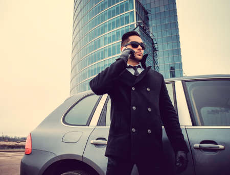 Stylish business male talking by smartphone near a car in the glass building background.の写真素材