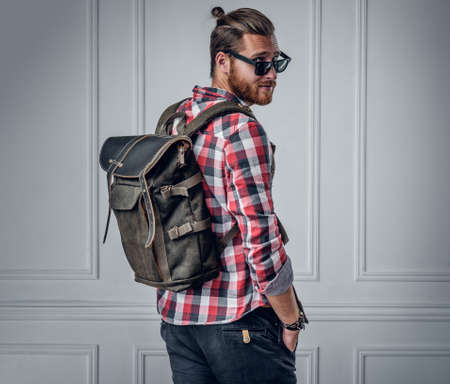 Stylish bearded hipster male showing leather rucksack on his back.