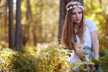 Freckled woman with circlet of flower on her head portrait in autumn forest in a day light.の写真素材