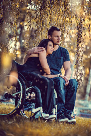 Handicapped young couple on two wheelchairs relaxing in autumn park.の写真素材