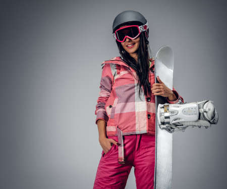 Portrait of active female in a pink ski costume holding a snowboard. Isolated on grey background.の写真素材