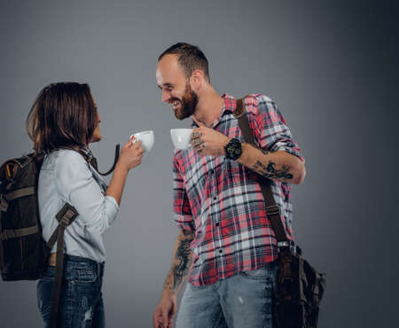 Image of two urban adults holding cups of coffee on grey background.