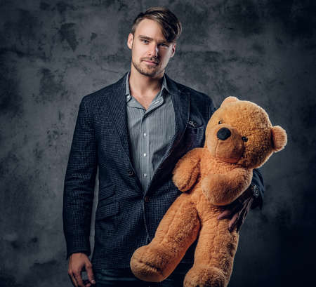 Male in a suit holding brown teddy bear on grey background.の写真素材