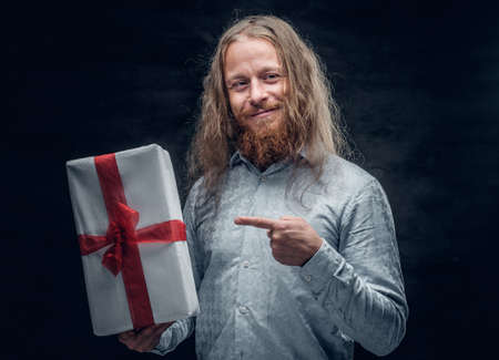Studio portrait of a positive bearded man with long hair holds the present box.の写真素材