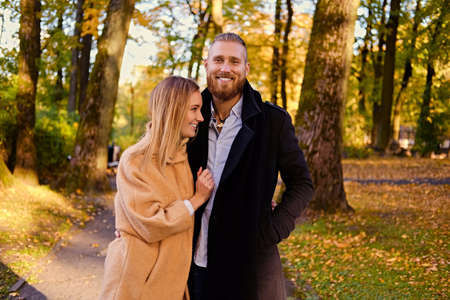 Autumn Love story. Redhead bearded male hugs the cute blonde female on the date in an autumn park.の写真素材