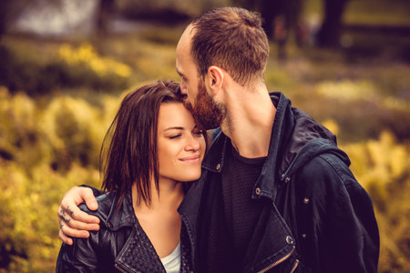 Love scene in autumn park - bearded male kissing cute happy female in a head.の写真素材