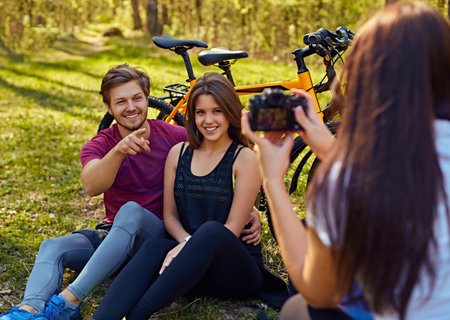 A woman taking pictures of sporty couple after bicycle ride in a forest.
