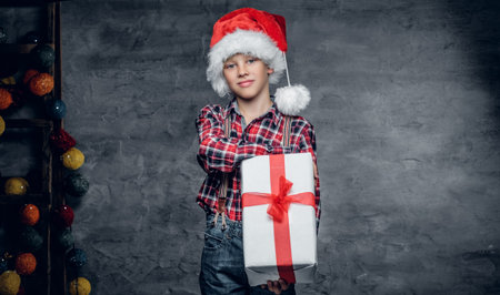 Cute teenage boy in Santa's hat holds gift box.の写真素材