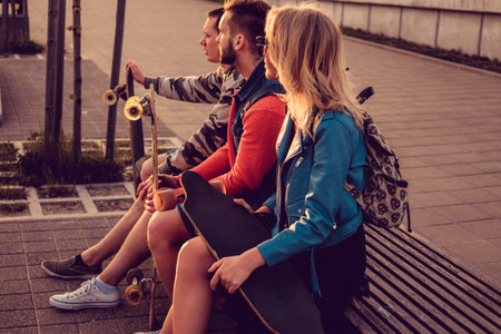 Friends, skateboard riders relaxing on a bench after riding at sunset.の写真素材