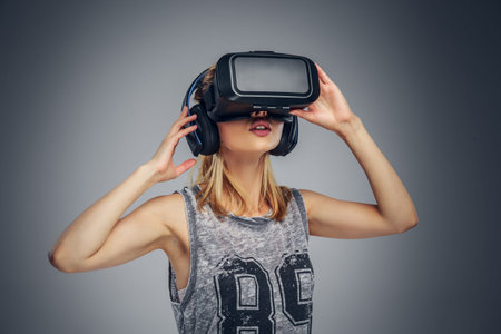 A Young blonde female wearing virtual reality glasses. Isolated on grey background.