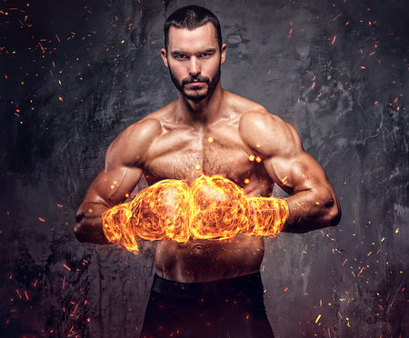Shirtless aggressive fighter with burning boxer gloves on grey background.の写真素材