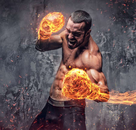Shirtless aggressive fighter with burning boxer gloves on grey background.の写真素材