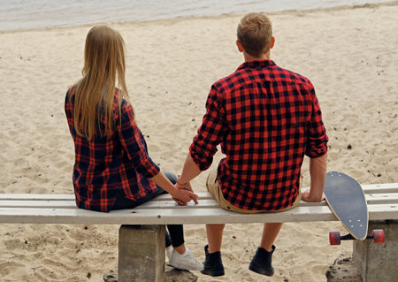Urban longboarder's couple from the back sitting on a bench on a beach.の写真素材