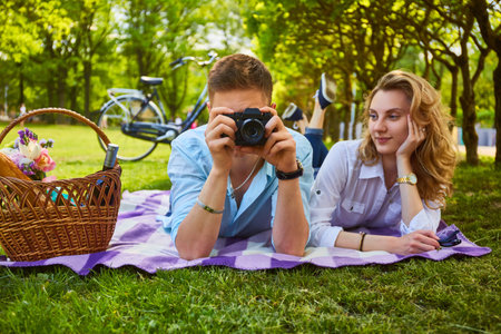 The attractive young couple using a compact photo camera at a picnic in a park.