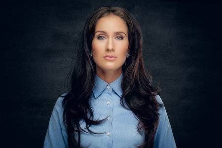Studio portrait of brunette female in a blue shirt on grey background.