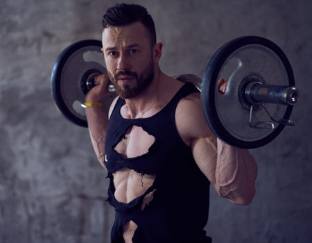 Portrait of abdominal bearded male in a shadow with barbell on his shoulders.