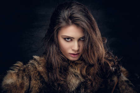 Portrait of a sensual brunette female dressed in a warm fur coat on grey background in a deep shadow.の写真素材