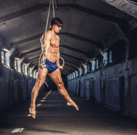Full body portrait of athletic gymnast exercising on stationary rings in a tunnel.の写真素材